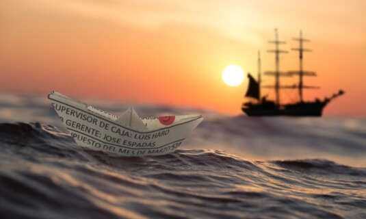 Papierschiff auf Wellen vor einem Segelschiff – Symbolbild Binnenschifffahrt