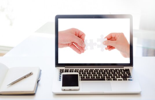 Laptop mit zwei Händen, die Puzzleteile zusammenfügen – Symbolbild digitale Zusammenarbeit